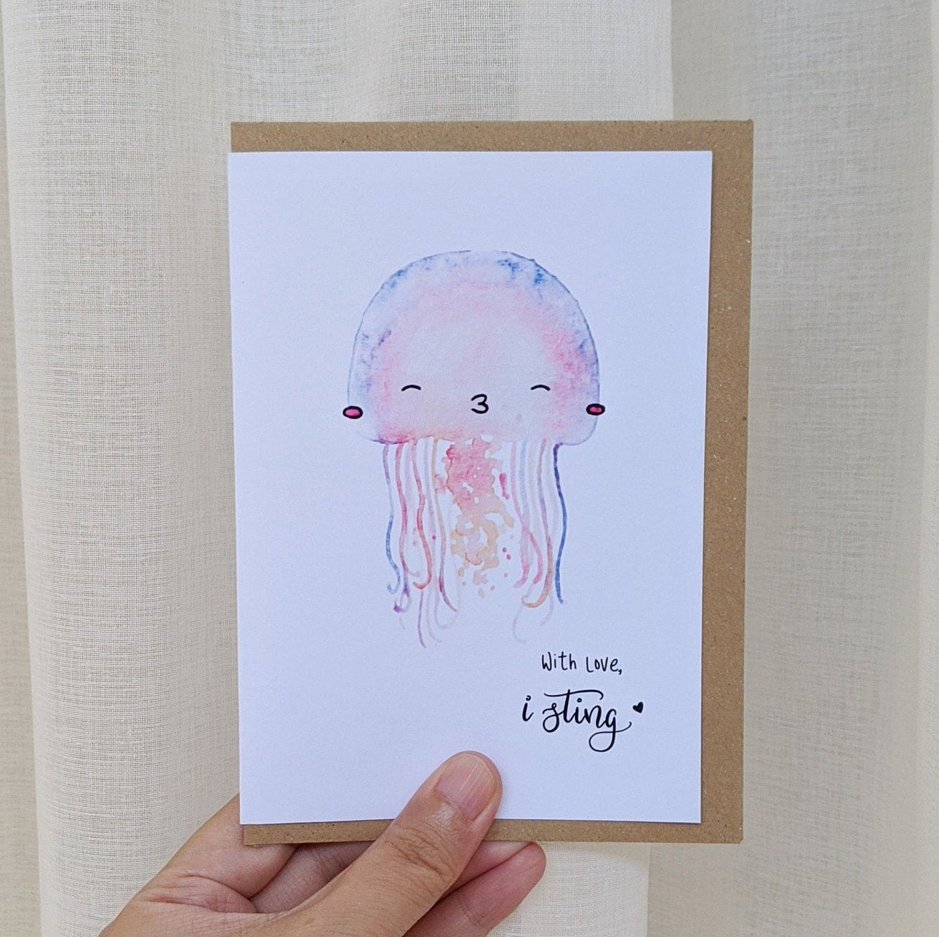 Greeting card of with watercolour illustration of a jellyfish kissing, signed off "with love, I sting" being held by a hand